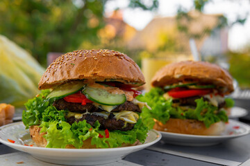 Big, nice hamburgers with a double patty, fresh vegetables and grilled meat. Sunny day outdoors. Concept of tasty street food. Selective focus