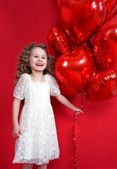 beautiful little girl smiles on a red background with heart-shaped balloon and gift box in her hands. The concept of love, present, Valentine's Day, February 14, March 8, mother's day, vertical photo