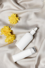 Two white bottles for cosmetics, hair, skin care products without a label on a beige satin background with yellow flowers for decoration