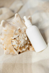 White jar or bottle for cosmetics, hair or care face products, without a label on a beige background with sea ​​shell. For beauty salons or cosmetics brands