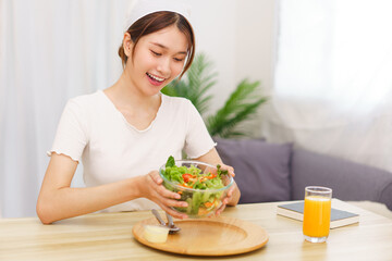 Obraz na płótnie Canvas Lifestyle in living room concept, Young Asian woman smiling and holding bowl of vegetable salad