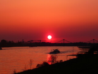 Sunset on the Rhine with a ship, a bridge and a container bridge behind Krefeld near Duisburg...