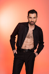Obraz premium sexy and bearded man with hairy chest standing with hands in pockets on pink.