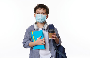 Fototapeta na wymiar Adorable positive teen boy, primary school student with schoolbag and copybook, holding out a disposable eco paper cup with hot drink at camera, isolated on background. Copy space