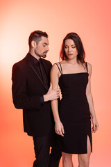 bearded man in black formal wear seducing brunette woman in dress on pink.