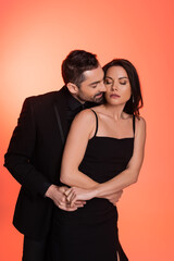 bearded man in suit seducing brunette woman in black dress on pink.