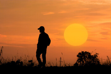a person with a backpack standing in a field as the sun sets in the distance.