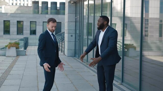 Two aggressive businessmen have bad conflict. Two angry businessmen swear, yell at each other standing downtown. Two men in suits emotionally deal with and insult each other. Different points of view.