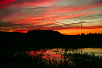 The sky after sunset is the background. A panorama of a colorful magnificent sunset in the countryside over hills, fields and a lake. sunset reflection in the lake. copy space. atmospheric photo