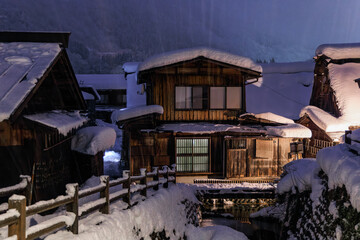 Fototapeta na wymiar Heavy snow falls on traditional wooden homes in Japanese village at night
