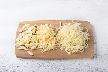 Wooden board with three types of grated cheese on a light blue background. Cooking delicious homemade pasta