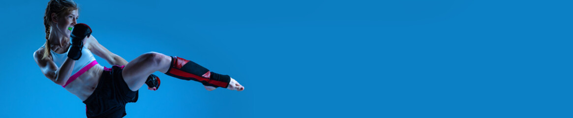 Dynamic image of young, teen, sportive girl, MMA fighter training over blue background. Banner, flyer