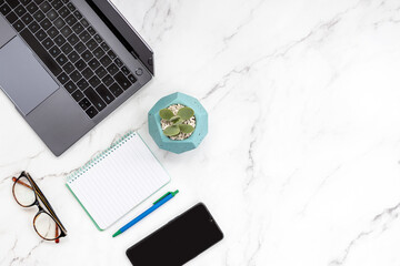 Top view of modern white marble layout of freelance worker with laptop, eyeglasses, smart phone, notepad and a succulent plant