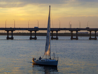 Fototapeta na wymiar a sailing yacht floats against the backdrop of a bright beautiful sky with a sunset near the bridge