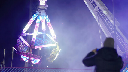 Person recording the amusement park bright giant pendulum swinging at night