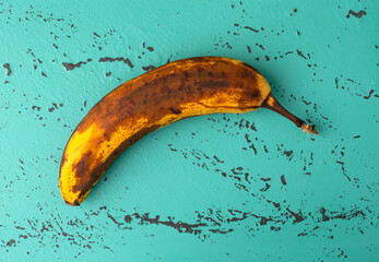 Top view of an overripe banana on a green and black mottled tabletop.