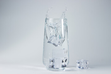 Ice cubes fall into a glass of water on a white background