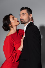 Sexy woman with burgundy lips hugging bearded boyfriend on grey background.