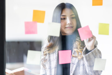 Business female employee with many conflicting priorities arranging sticky notes commenting and brainstorming on work priorities colleague in a modern office.
