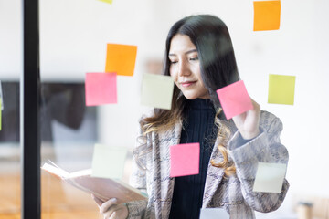 Business female employee with many conflicting priorities arranging sticky notes commenting and...