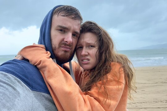 Portrait of unhappy depressed frozen trembling guy and girl, young shivering from cold sad upset couple on the sea beach, suffering from bad weather on summer vacation  - Powered by Adobe