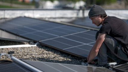Male team engineers installing stand-alone solar photovoltaic panel system. Electricians mounting blue solar module on roof of company roof. Alternative energy concept
