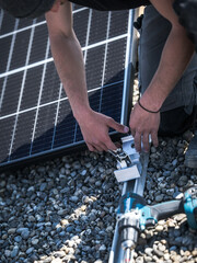 Male team engineers installing stand-alone solar photovoltaic panel system. Electricians mounting blue solar module on roof of company roof. Alternative energy concept