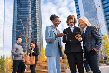 Multi-ethnic business colleagues or executives, looking at technology, glass office buildings