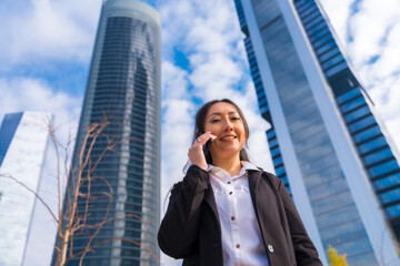 Latin businesswoman corporate portrait, business park, soft on phone next to skyscraper