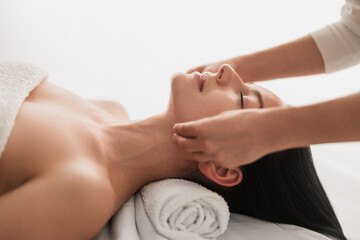 Anonymous therapist massaging face of female client lying with closed eyes