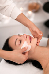 Obraz na płótnie Canvas Crop beautician doing face massage with gua sha to female customer