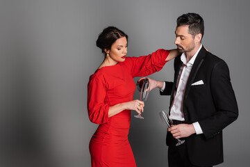 Elegant man in suit pouring champagne in glass of girlfriend in dress on grey background.