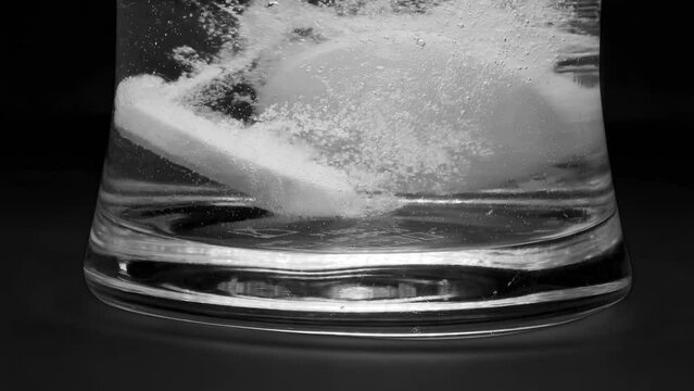 Macro close up to a glass while dropping two effervescent antacid pain reliever tablets to a glass of water