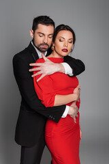 Bearded man in suit hugging seductive woman with burgundy lips isolated on grey.