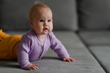 Caucasian little baby is lying on his stomach on a gray sofa