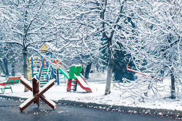 Snow-covered playground in the courtyard of a residential building in Lviv Ukraine. An anti-tank hedgehog is installed nearby. War in Ukraine.  © Светлана Мищенко