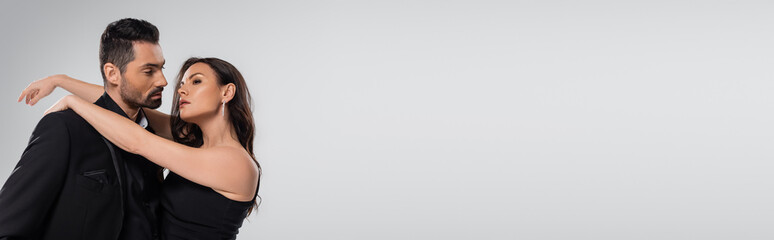 dreamy woman hugging bearded man in black suit isolated on grey, banner.