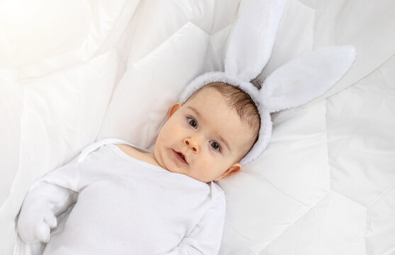 cute little baby boy with bunny rabbit ears headband lies lying on blanket chewing soft toy for teething period.adorable toddler infant smiling have fun wide banner easter holiday year of rabbit