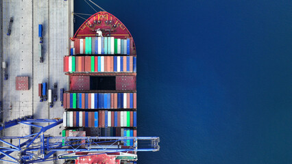 Aerial drone top down photo of industrial cargo container ship being loaded by large cranes in...