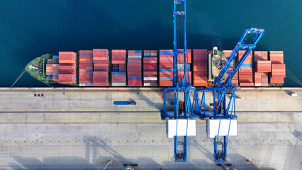 Aerial top down photo of industrial cargo container ship being loaded by large cranes in logistics...