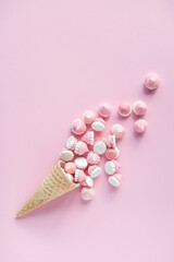 Multicolored pink and white meringues in waffle cookies lie scattered on a pink background