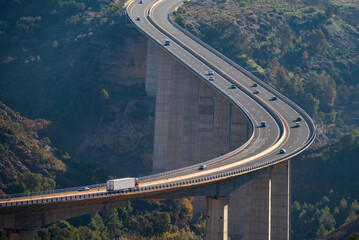 Huge viaduct crossing a ravine with a truck with a refrigerated semi-trailer and several vehicles circulating on the road, elevated view.