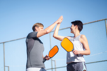 Laughing couple playing pickleball game, hitting pickleball yellow ball with paddle, outdoor sport...