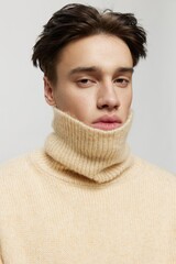 Portrait photo. vertical studio. close-up photo.Cute young man with dark combed back short curly hair in a beige sweater with a high neck stands on a gray background vertical studio photo
