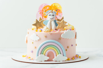 Unicorn cake with pink cream cheese frosting decorated with mastic rainbow, multicolored caramel candies and unicorn shaped figure on top. Birthday cake for a little girl on the white background