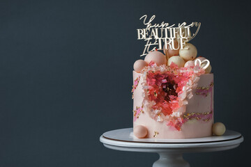 Luxury anniversary cake with pink cream cheese frosting decorated with golden petals on the dark...