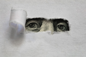 Benjamin Franklin peeking through torn white paper