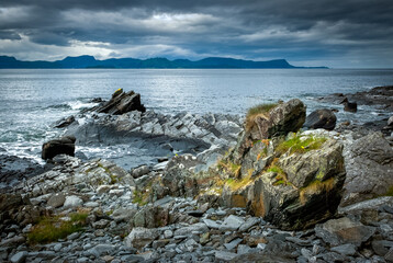Fototapeta na wymiar Jagged rocks with moss adorn the rugged coastline under a stormy sky at evening.