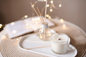 Scented candle with liquid home fragrance on tray at coffee table on knit cloth textile. Cozy...