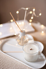 Home liquid perfume in glass bottle with bamboo sticks and scented candle on tray at coffee table in room. Cozy atmosphere.